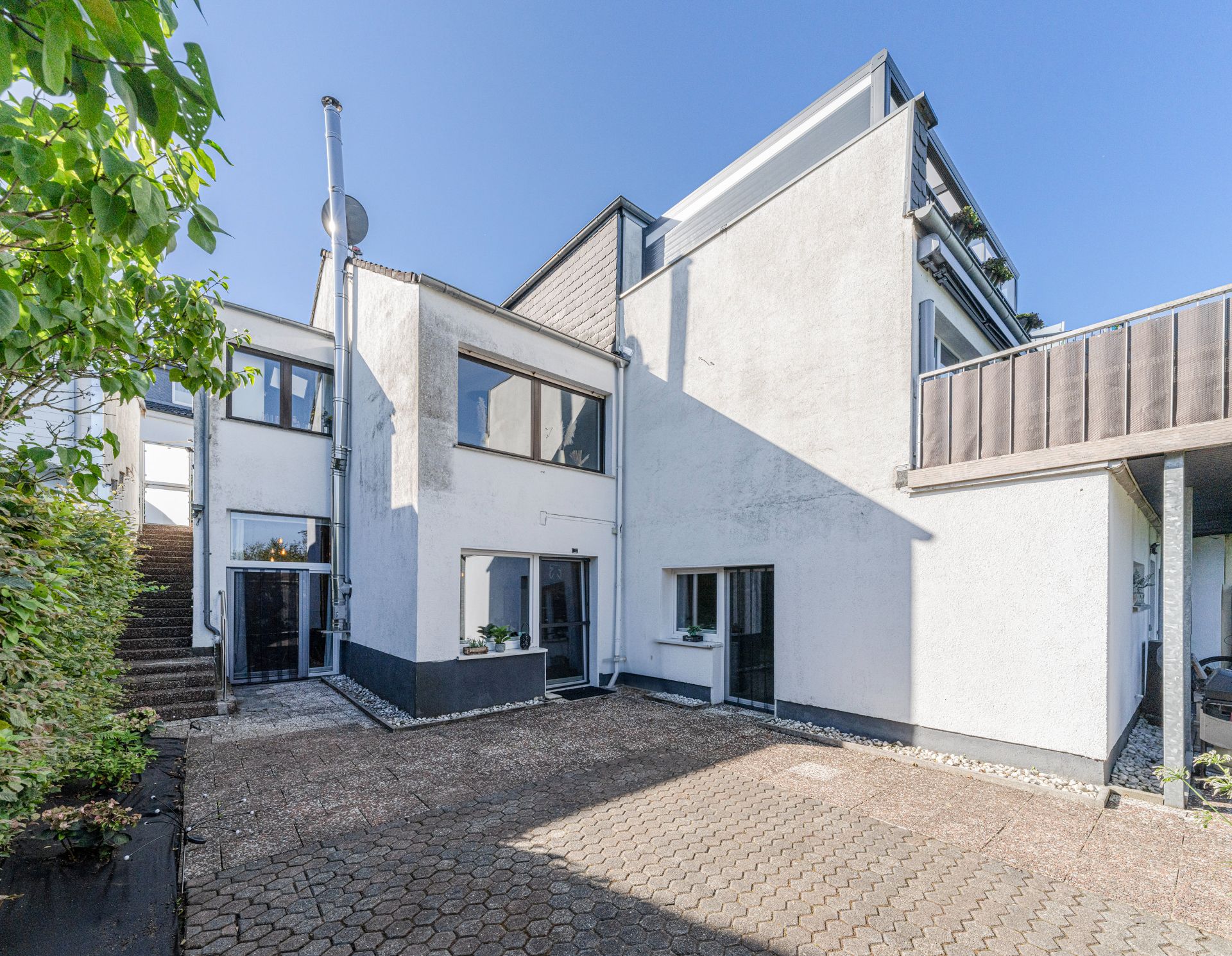 Moderner weißer Wohnhaus-Außenbereich mit Terrasse, großen Fenstern und Treppe.