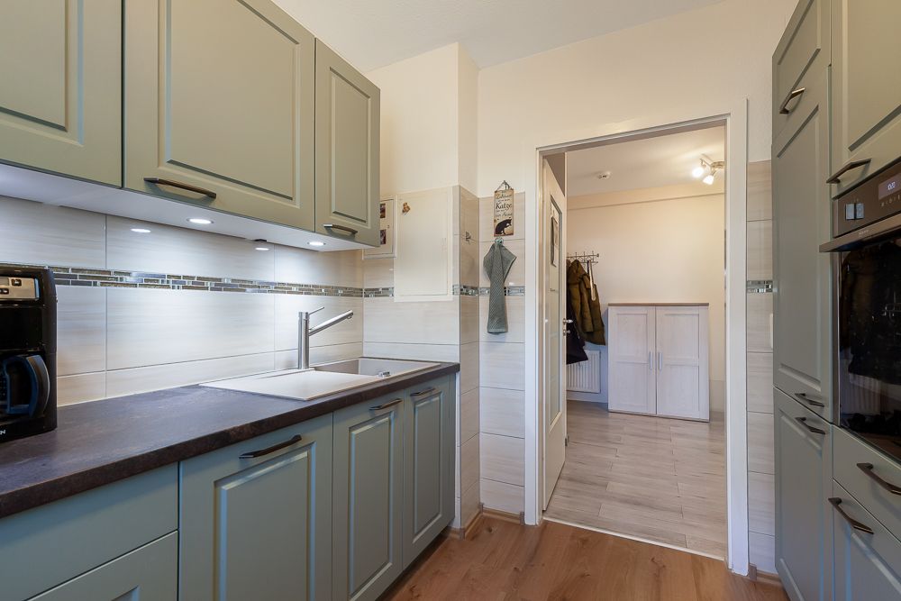 Moderne, schmale Küche mit grünen Schränken, Spüle und Blick in einen Flur mit Garderobe.