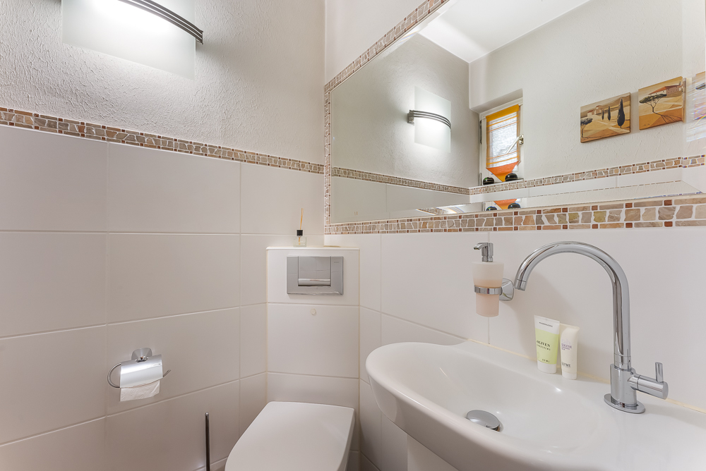 Modernes Badezimmer mit Waschbecken, Toilette, Spiegel und Wandbeleuchtung.