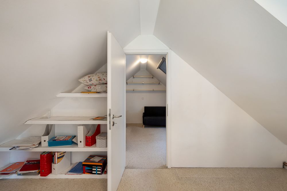 Dachzimmer mit offenem Regal auf der linken Seite und Sofa im nächsten Raum.