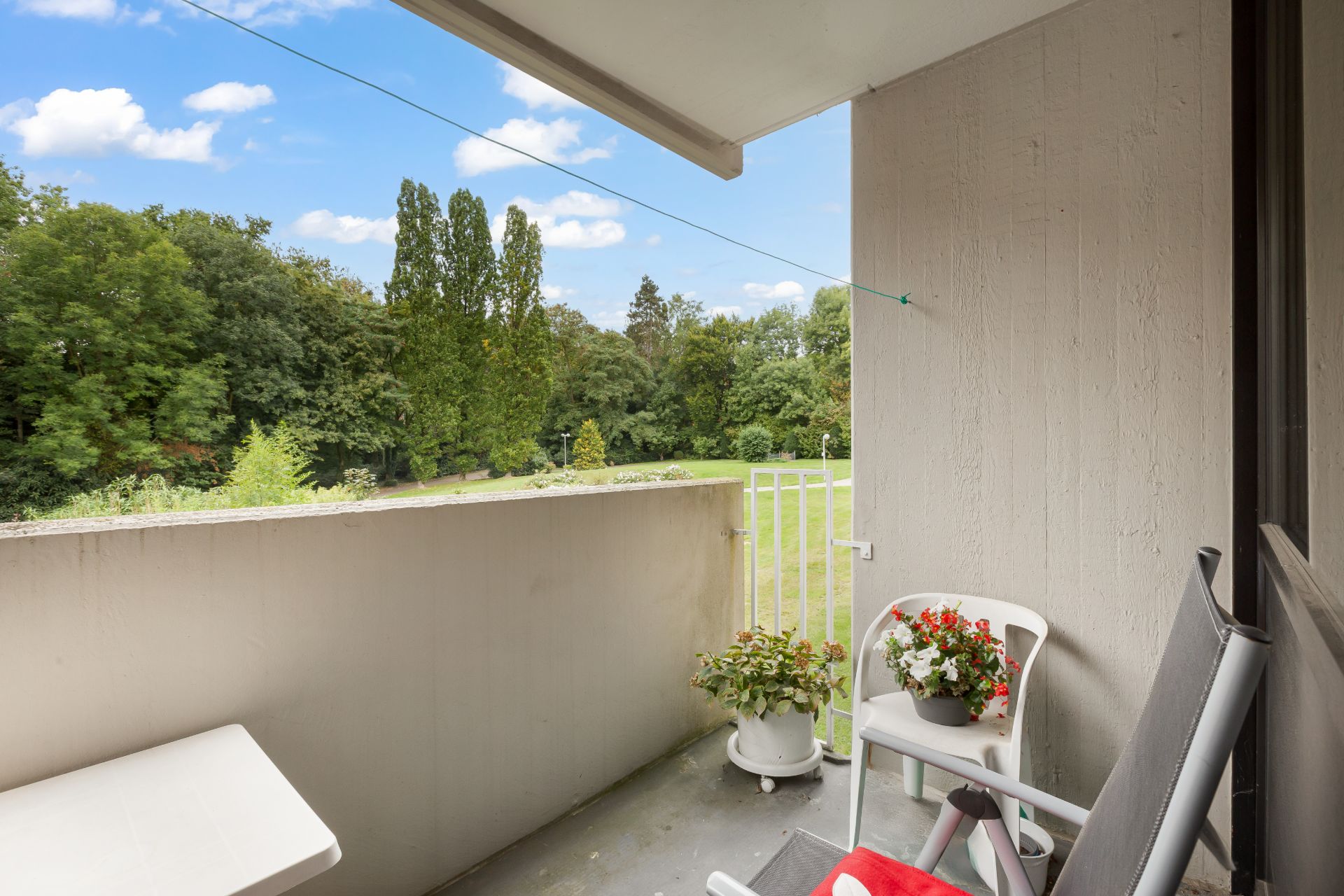 Balkon mit zwei Stühlen, Blumentöpfen und Blick auf grünen Garten.