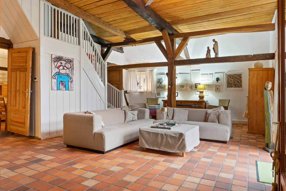Wohnzimmer mit Ecksofa, Couchtisch und sichtbaren Holzbalken an Decke und Wänden.