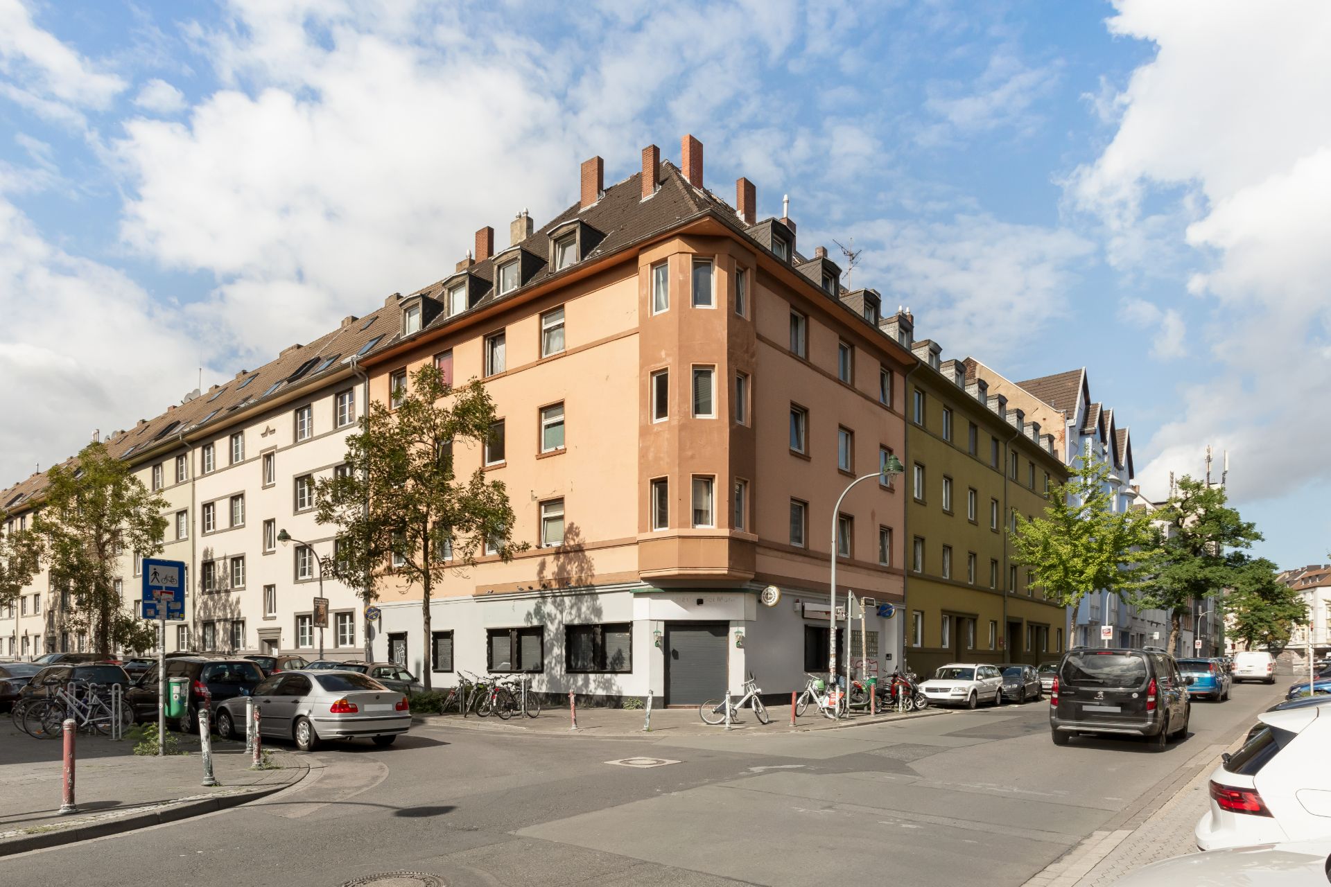 Eckwohnhaus mit mehreren Etagen, geparkte Autos und Fahrräder an der Straße.
