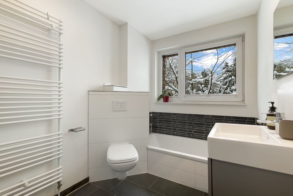 Modernes Badezimmer mit Badewanne, wandhängendem WC, Fenster und Handtuchheizkörper.