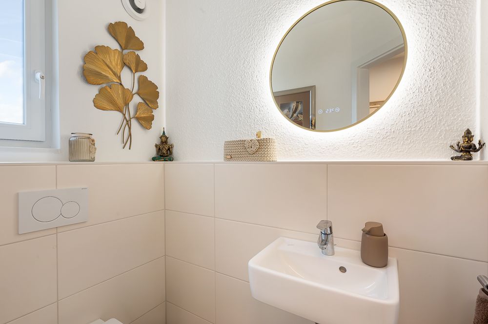 Kleines Badezimmer mit rundem Spiegel, Waschbecken und Dekoration an der Wand.