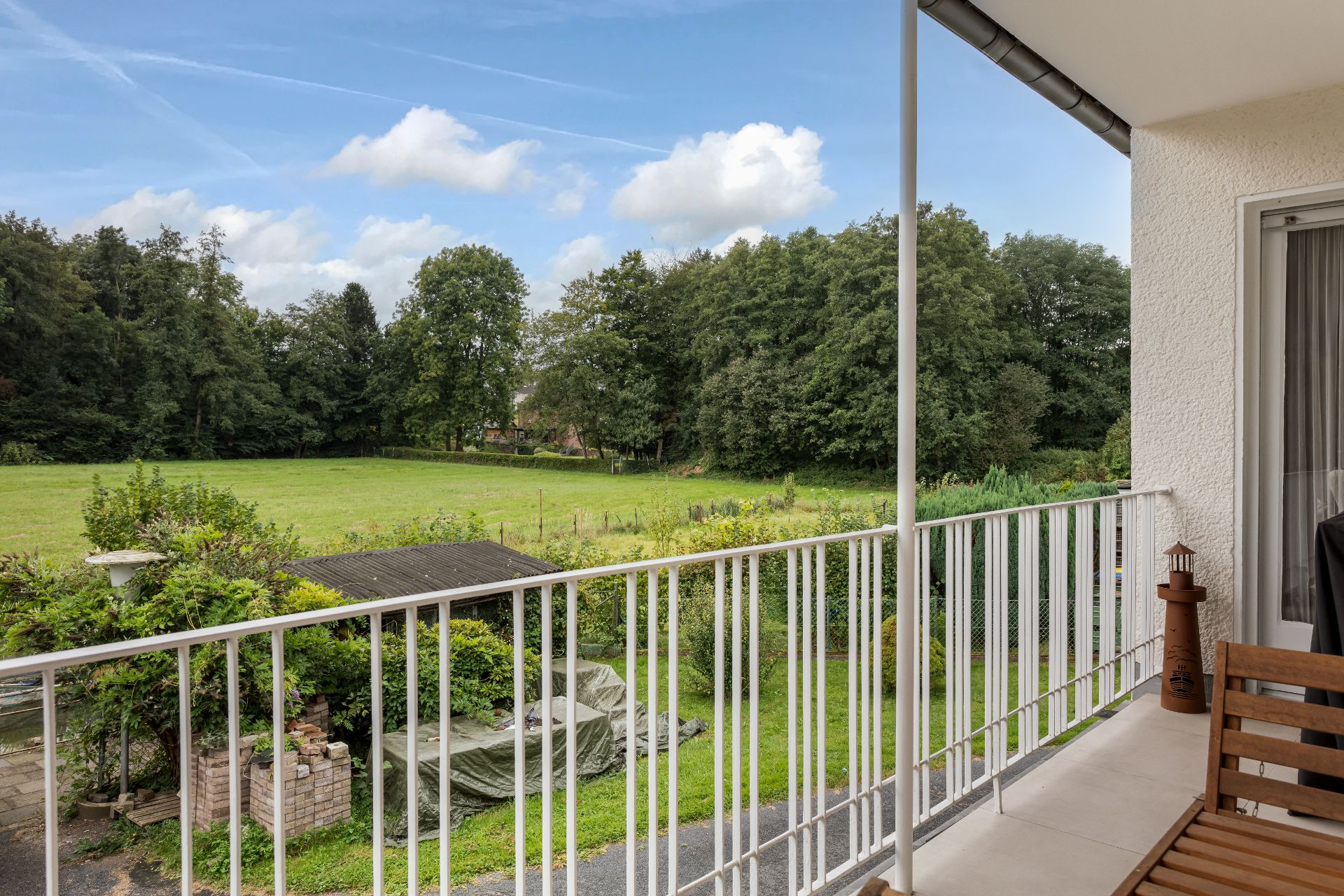 Balkon mit weißem Geländer und Blick auf grünen Garten und Wiese mit Bäumen.