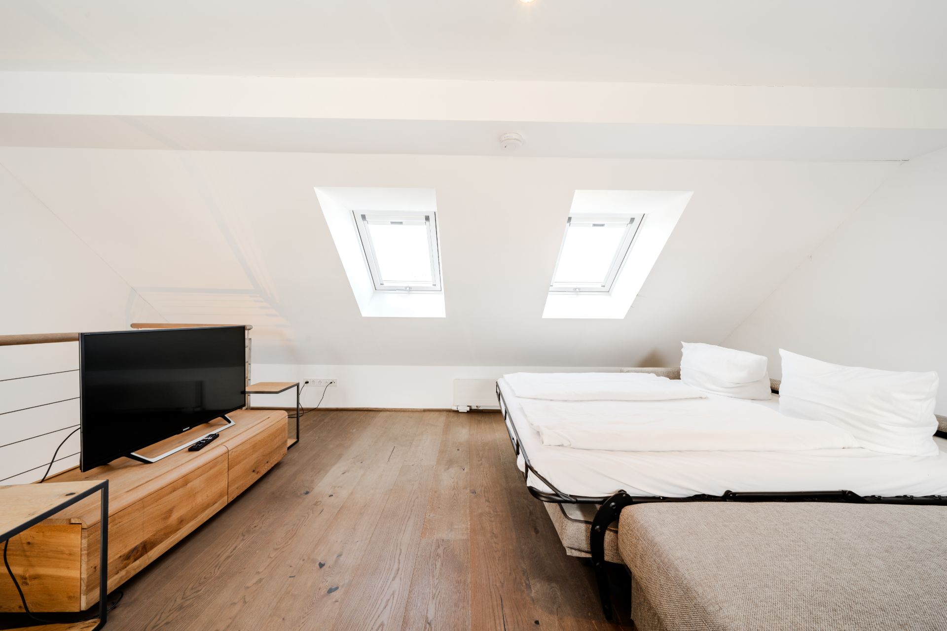 Helles Schlafzimmer mit Doppelbett, Fernseher und zwei Dachfenstern auf Holzboden.