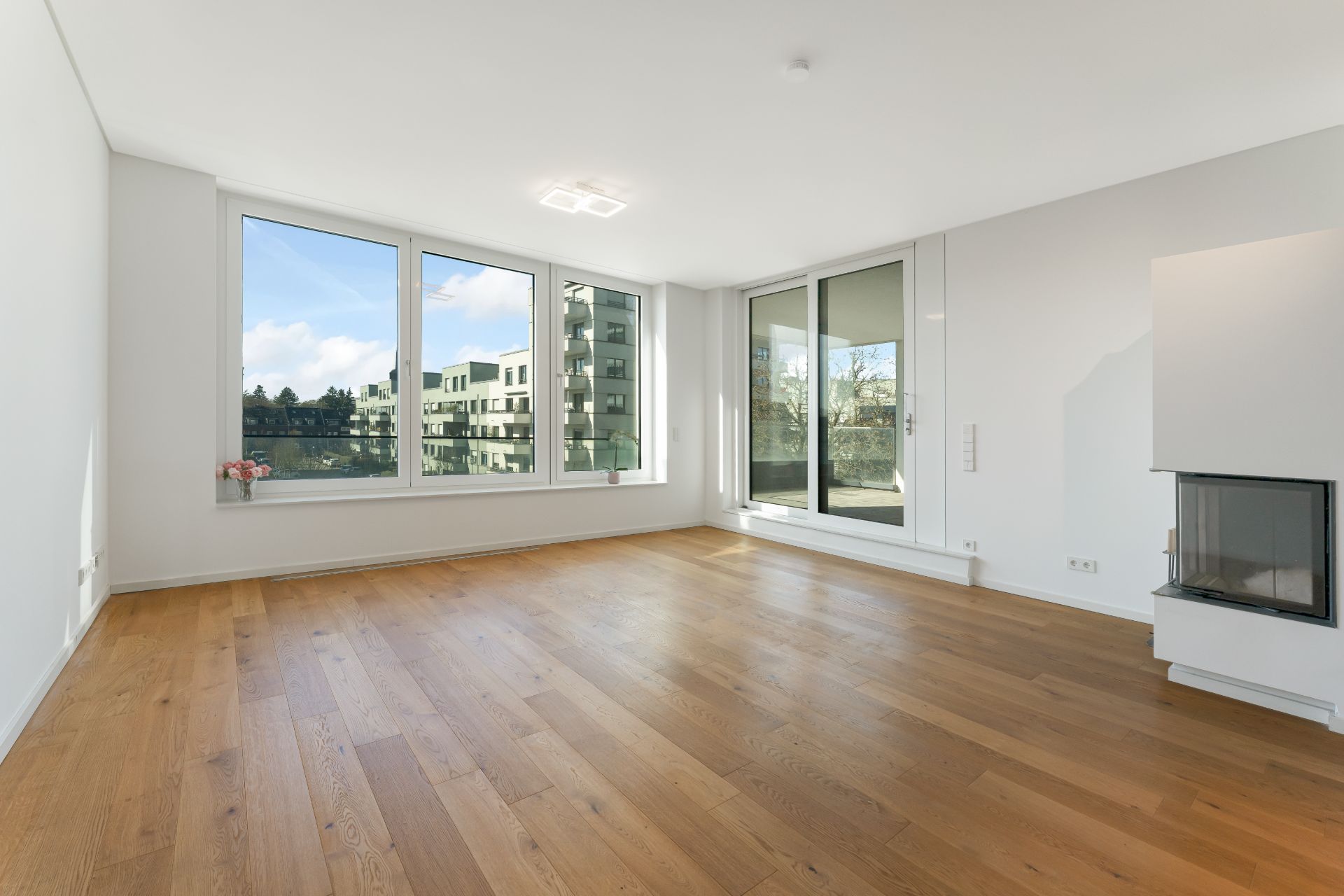 Helles Wohnzimmer mit Holzfußboden, großen Fenstern und einem Kamin.