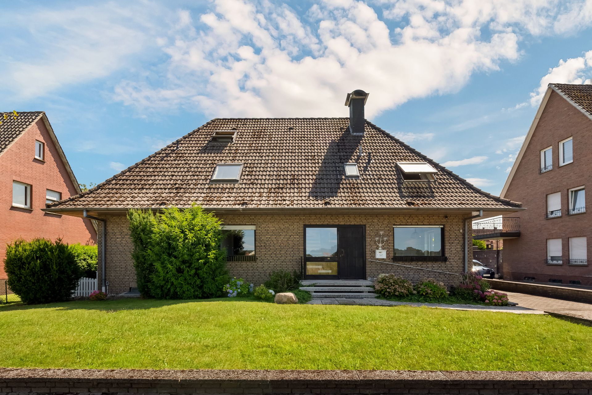 Einfamilienhaus mit Satteldach, Vorgarten und großen Fenstern an der Vorderseite.