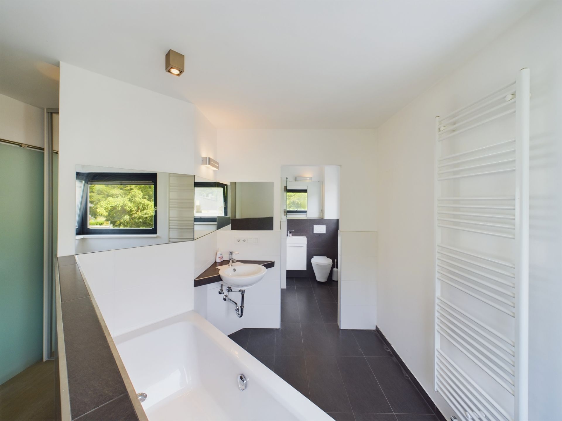 Modernes Badezimmer mit Badewanne, Waschbecken, WC, Fenster und Handtuchheizkörper.
