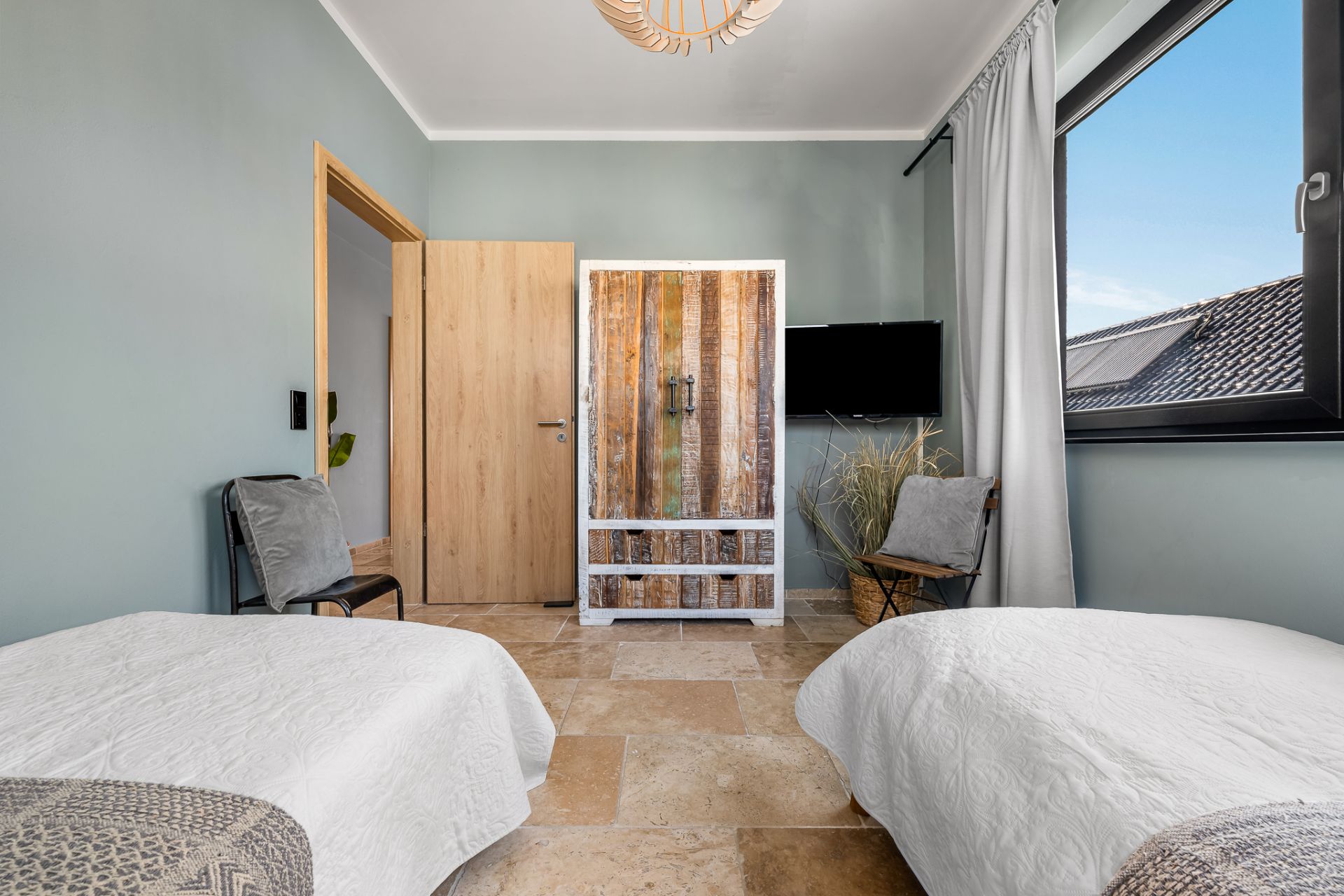 Zweibettzimmer mit zwei Einzelbetten, rustikalem Schrank und großem Fenster.
