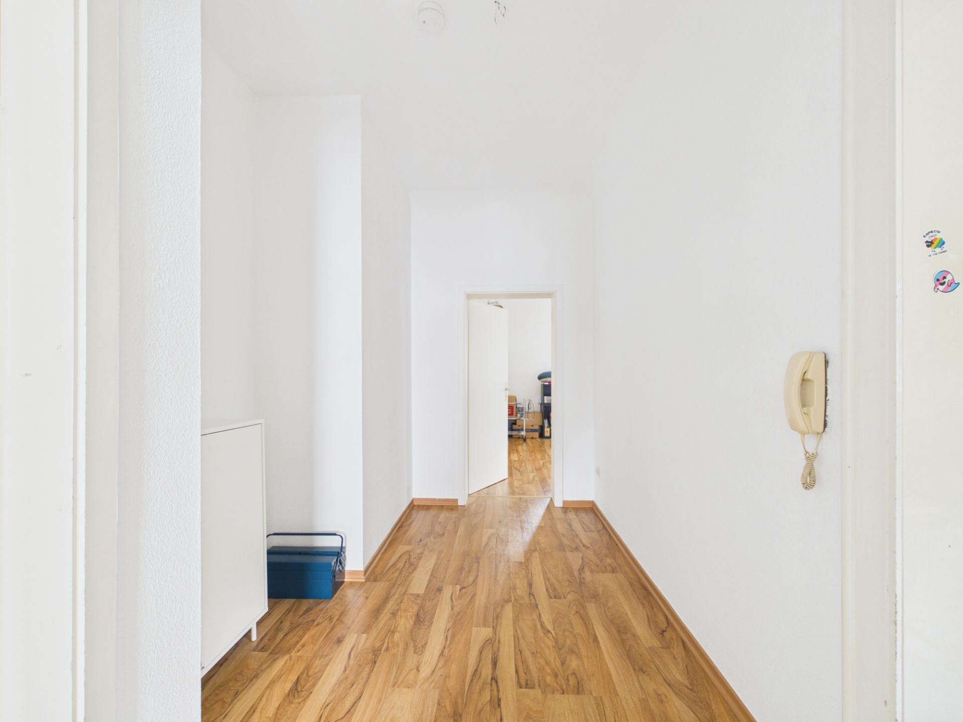 Heller Flur mit Holzfußboden, weißen Wänden und Gegensprechanlage an der Wand.