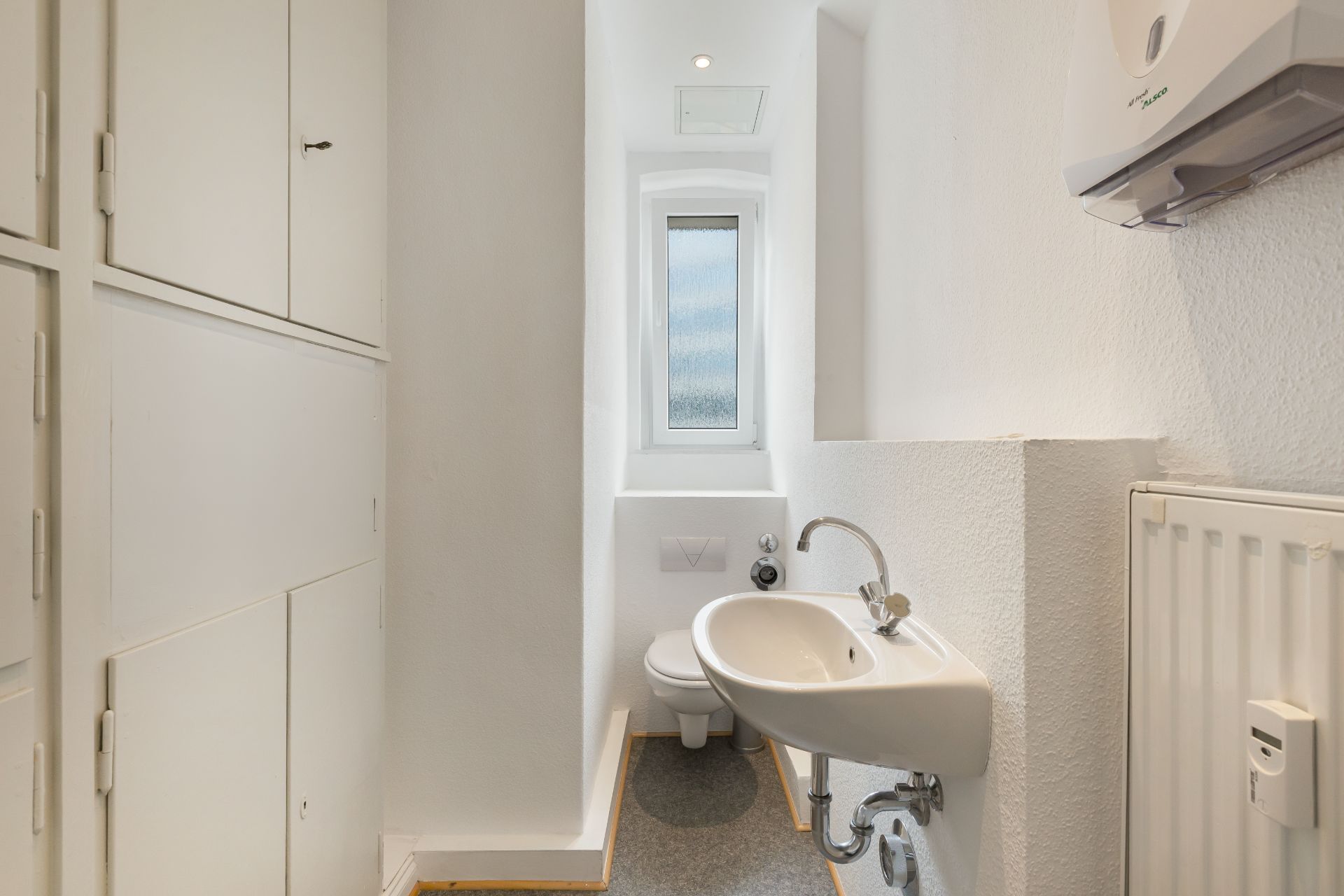 Kleines, schmales Badezimmer mit Toilette, Waschbecken und Fenster.