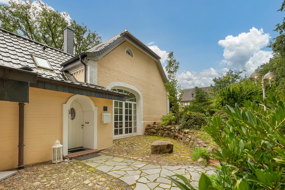 Eingang eines gelben Hauses mit Rundbogentür, Garten und Steinweg im Vordergrund.