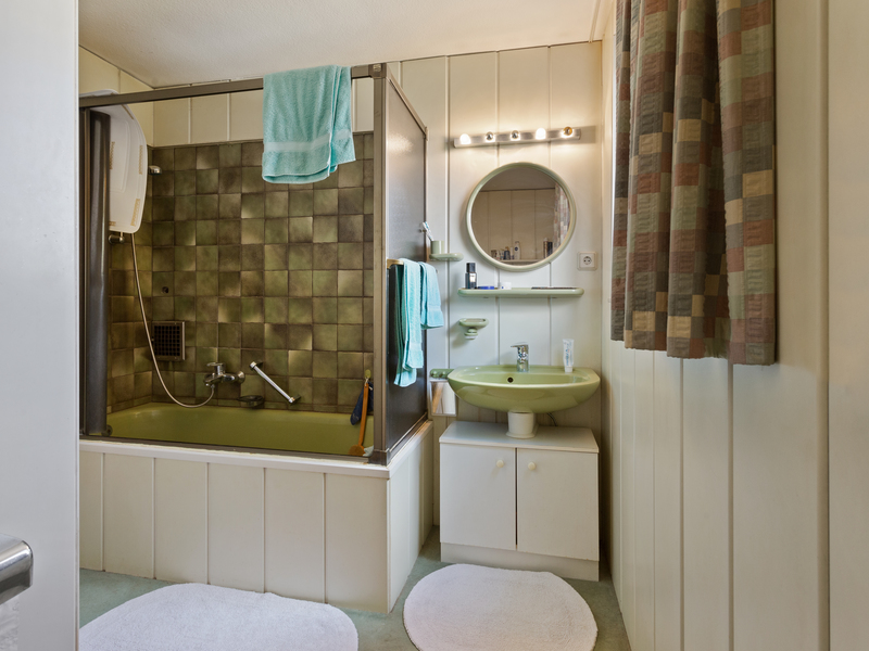 Badezimmer mit grüner Badewanne, grünem Waschbecken, Spiegel und weißen Teppichen.