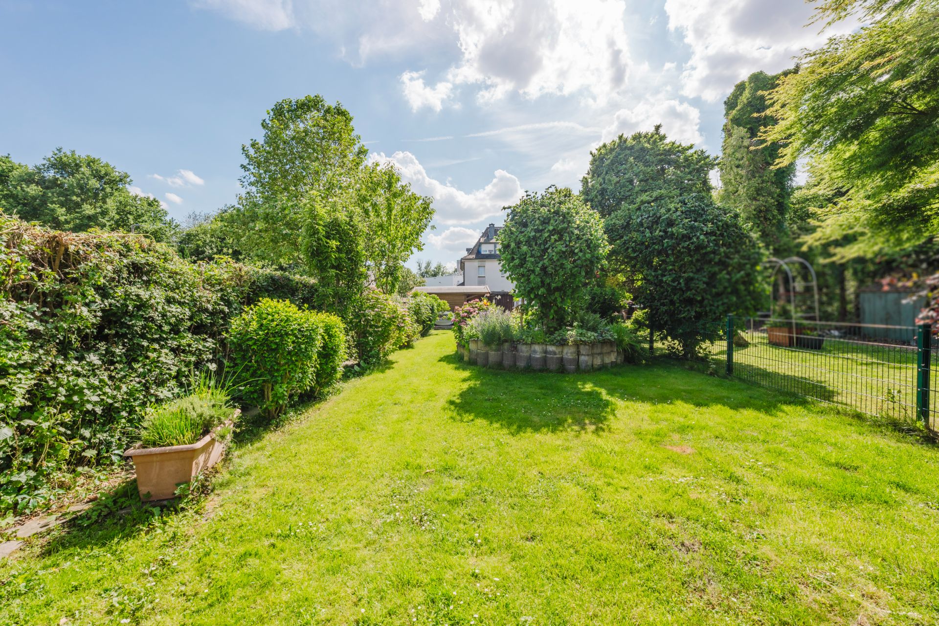 Grüner Garten mit Rasen, Büschen, Bäumen und Blumenbeet an einem sonnigen Tag.