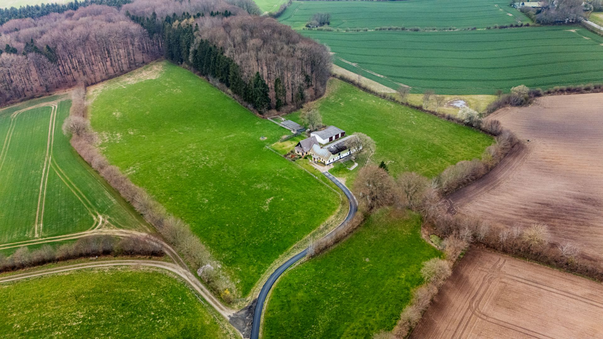Luftaufnahme eines Hauses auf großem Grundstück mit Feldern und Wäldern.