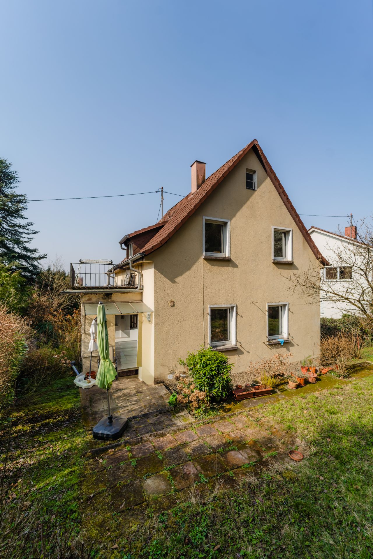 Zweistöckiges Wohnhaus mit Satteldach, Terrasse, Garten und einigen Blumentöpfen.