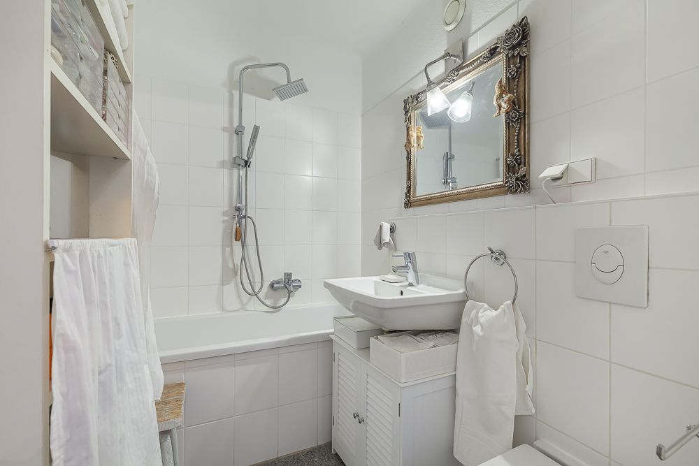 Helles Badezimmer mit Badewanne, Waschbecken, Spiegel und Regal mit Handtüchern.