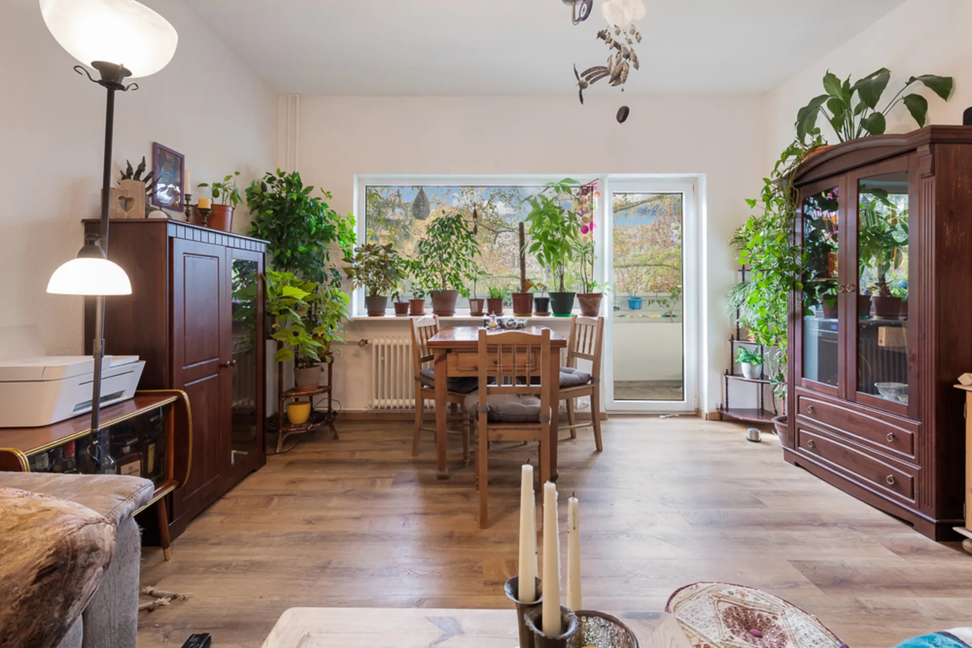 Wohnzimmer mit Holzboden, Esstisch, vielen Zimmerpflanzen und großen Fenstern.
