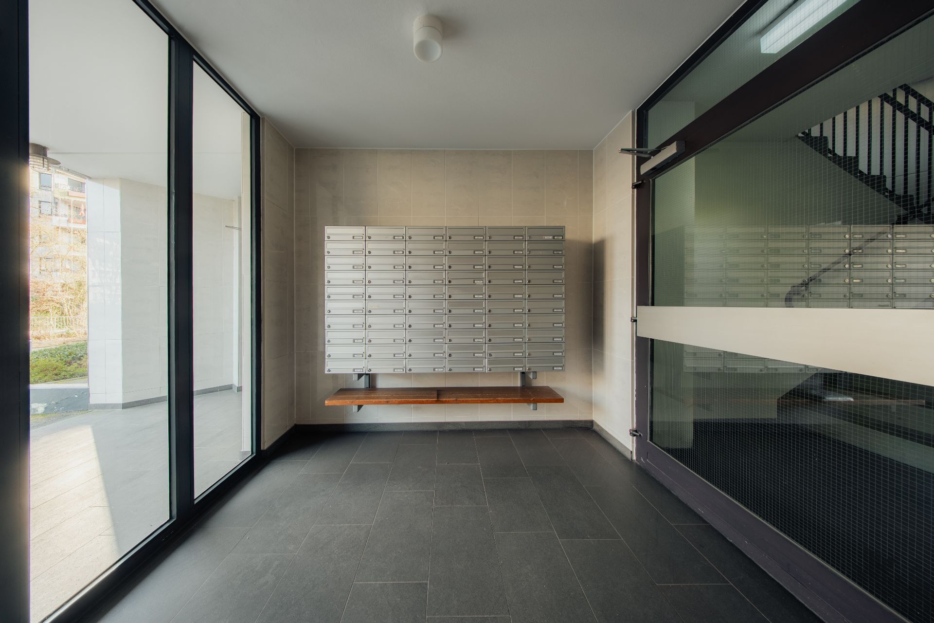 Raum mit vielen Briefkästen an der Wand, Glastüren und einer Bank darunter.