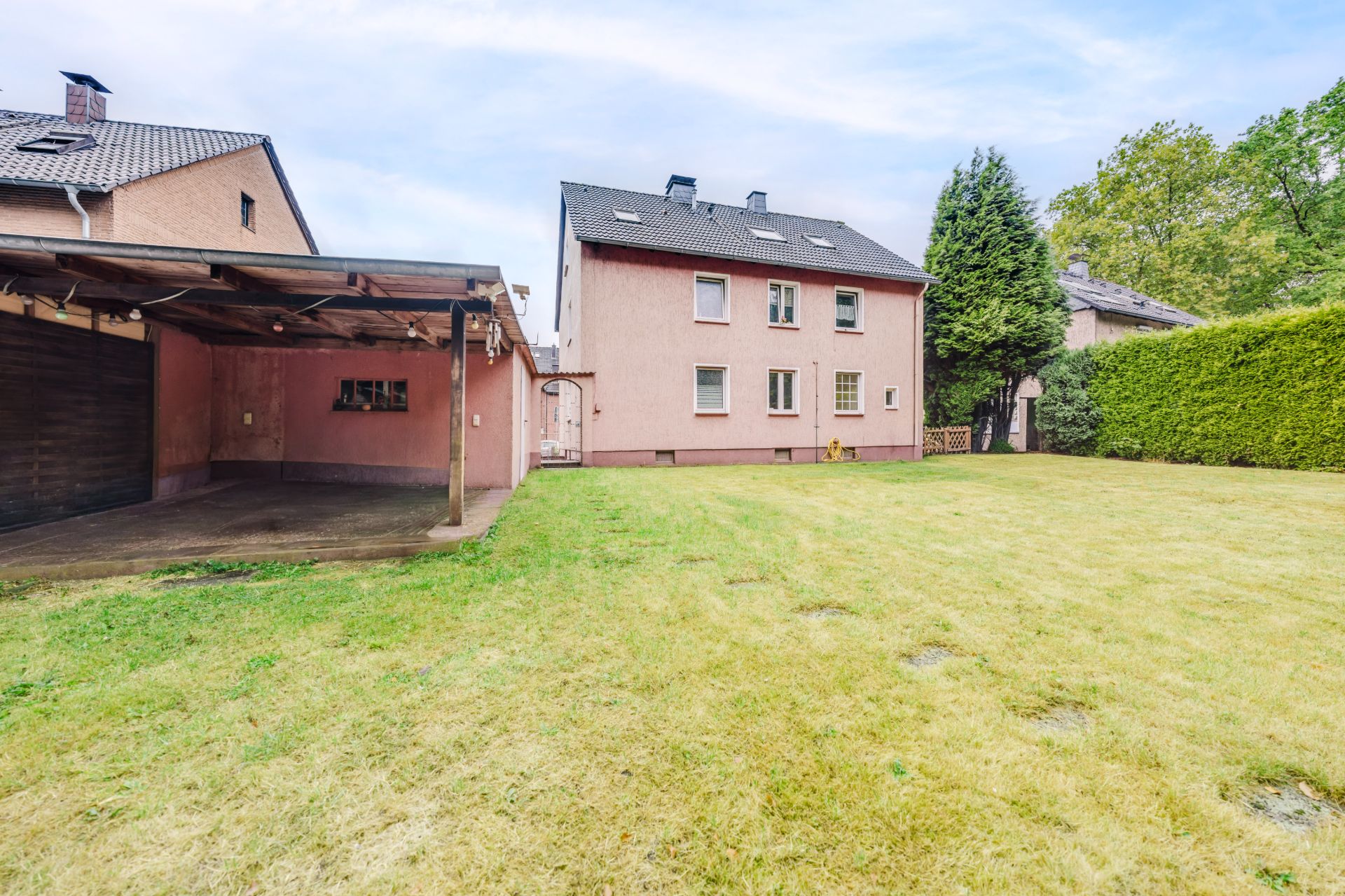 Hinteransicht eines Wohnhauses mit großem Rasen und überdachtem Carport auf der linken Seite.