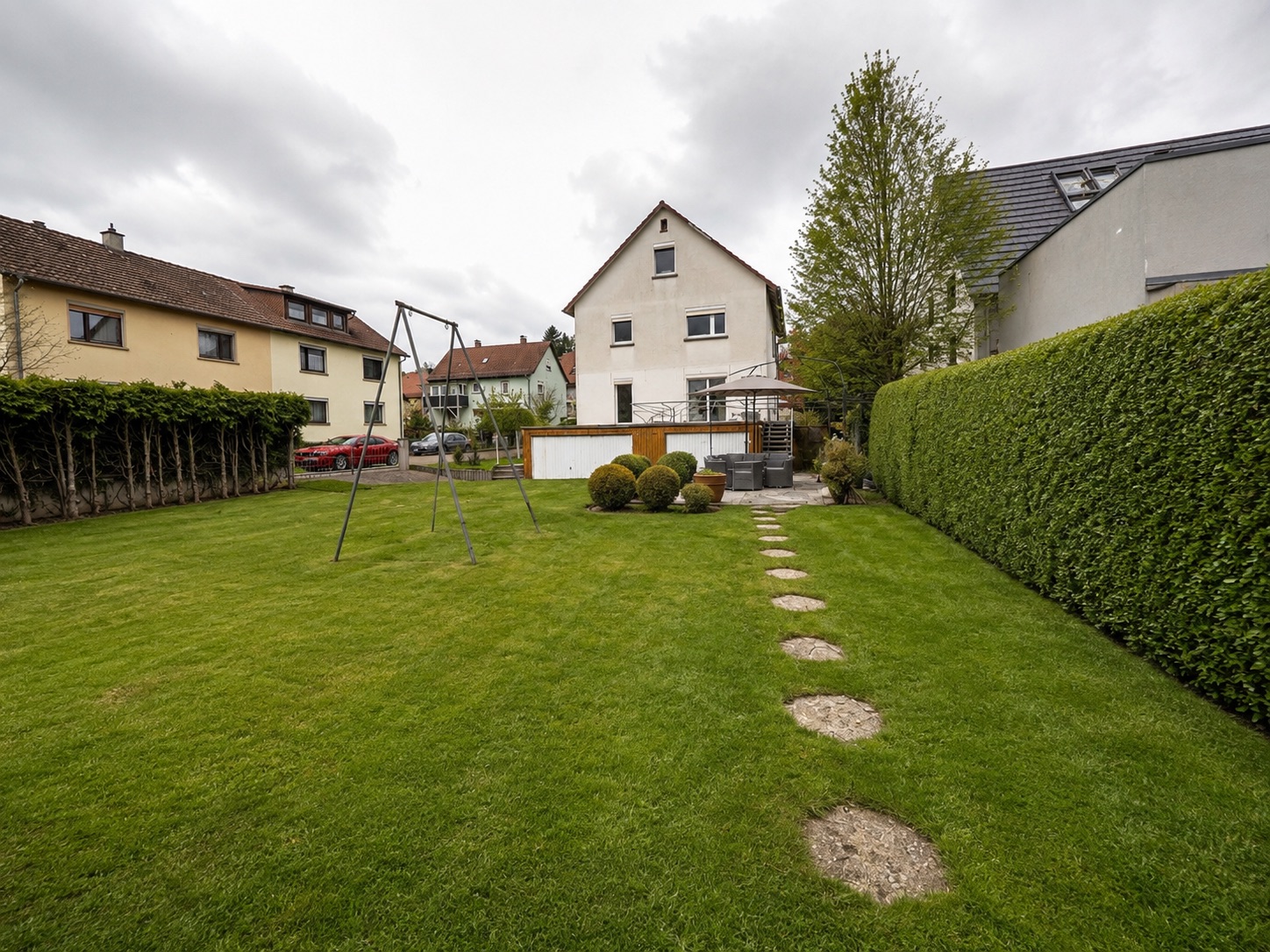 Großer Garten mit Rasen, Steinen als Weg, Schaukel und Wohnhaus im Hintergrund.