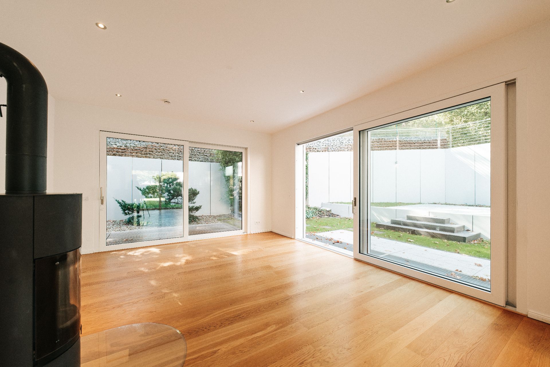 Helles Wohnzimmer mit Holzfußboden, großem Kamin und zwei großen Glasschiebetüren zum Garten.