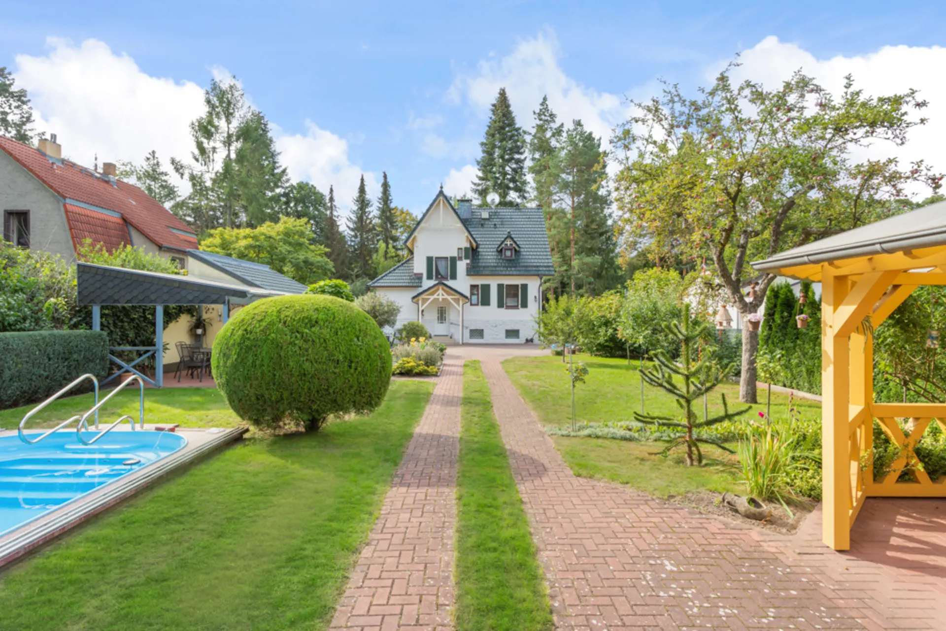 Gepflegter Garten mit Pool, Gartenhaus und Gehweg zu einem weißen Wohnhaus.