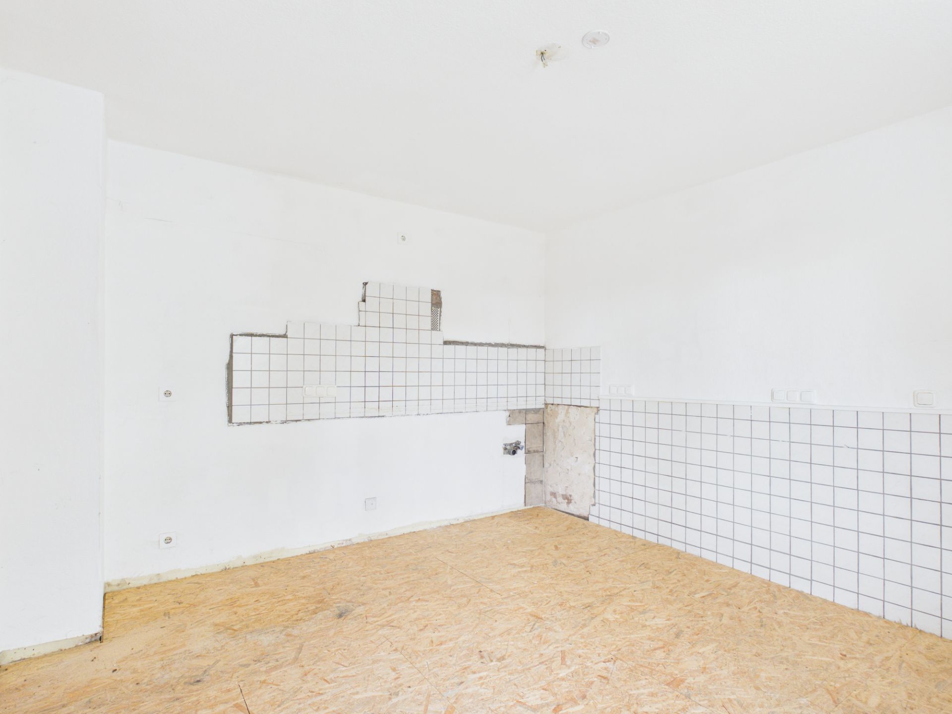 Leerer Raum mit teilweise gefliester Wand und einfachem Holzfußboden.