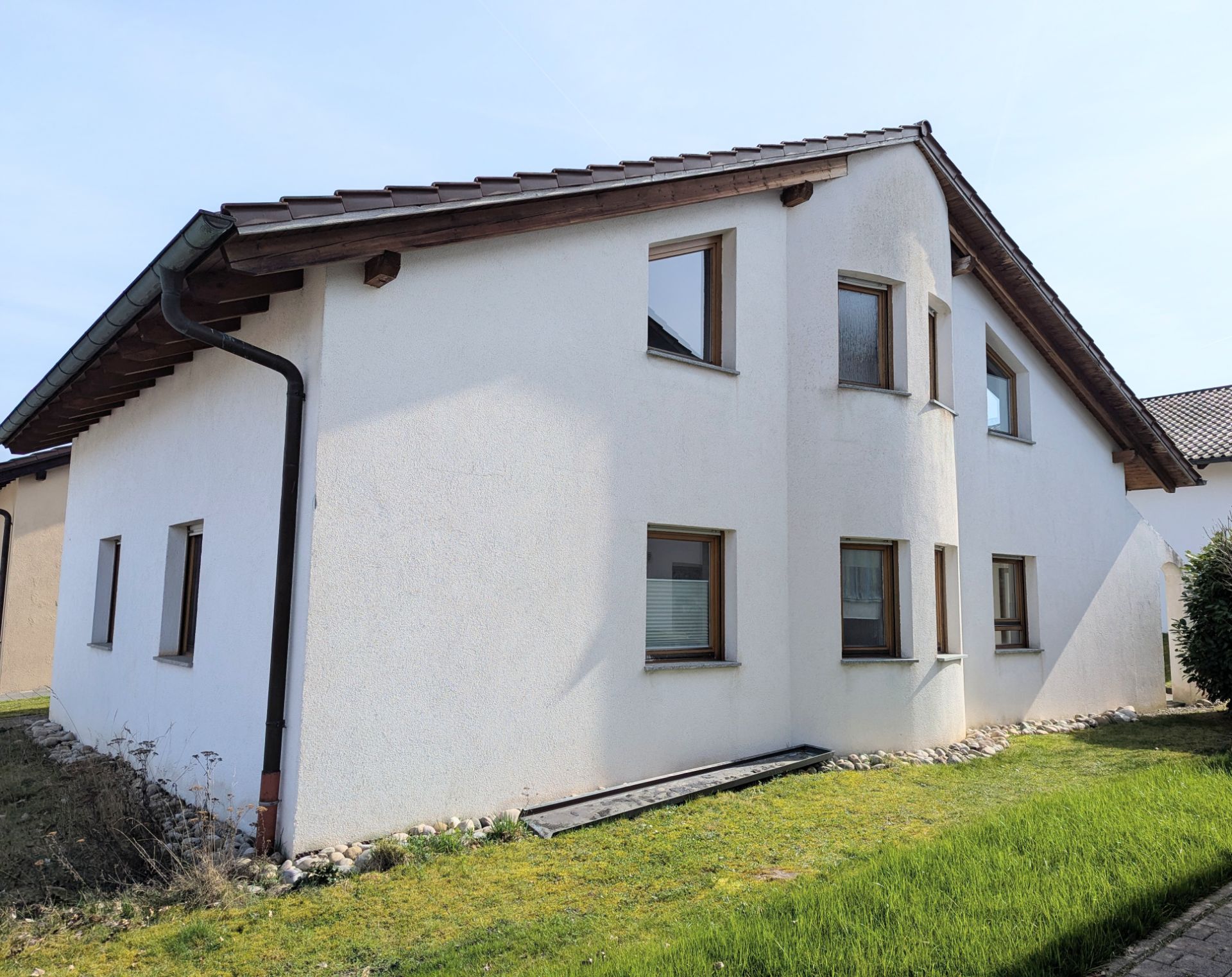 Weißes Einfamilienhaus mit Satteldach und mehreren Fenstern, umgeben von Rasen.