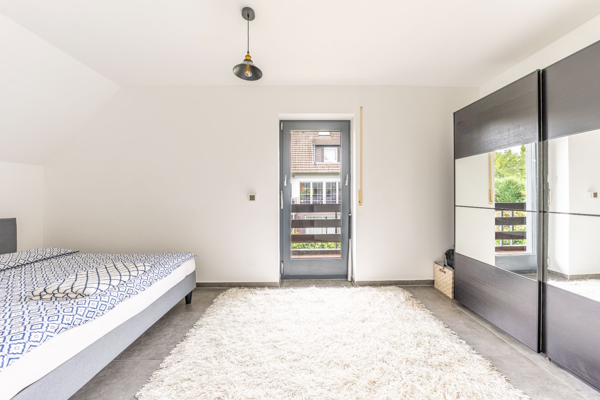 Helles Schlafzimmer mit Bett, großem Teppich, Kleiderschrank und Tür zum Balkon.