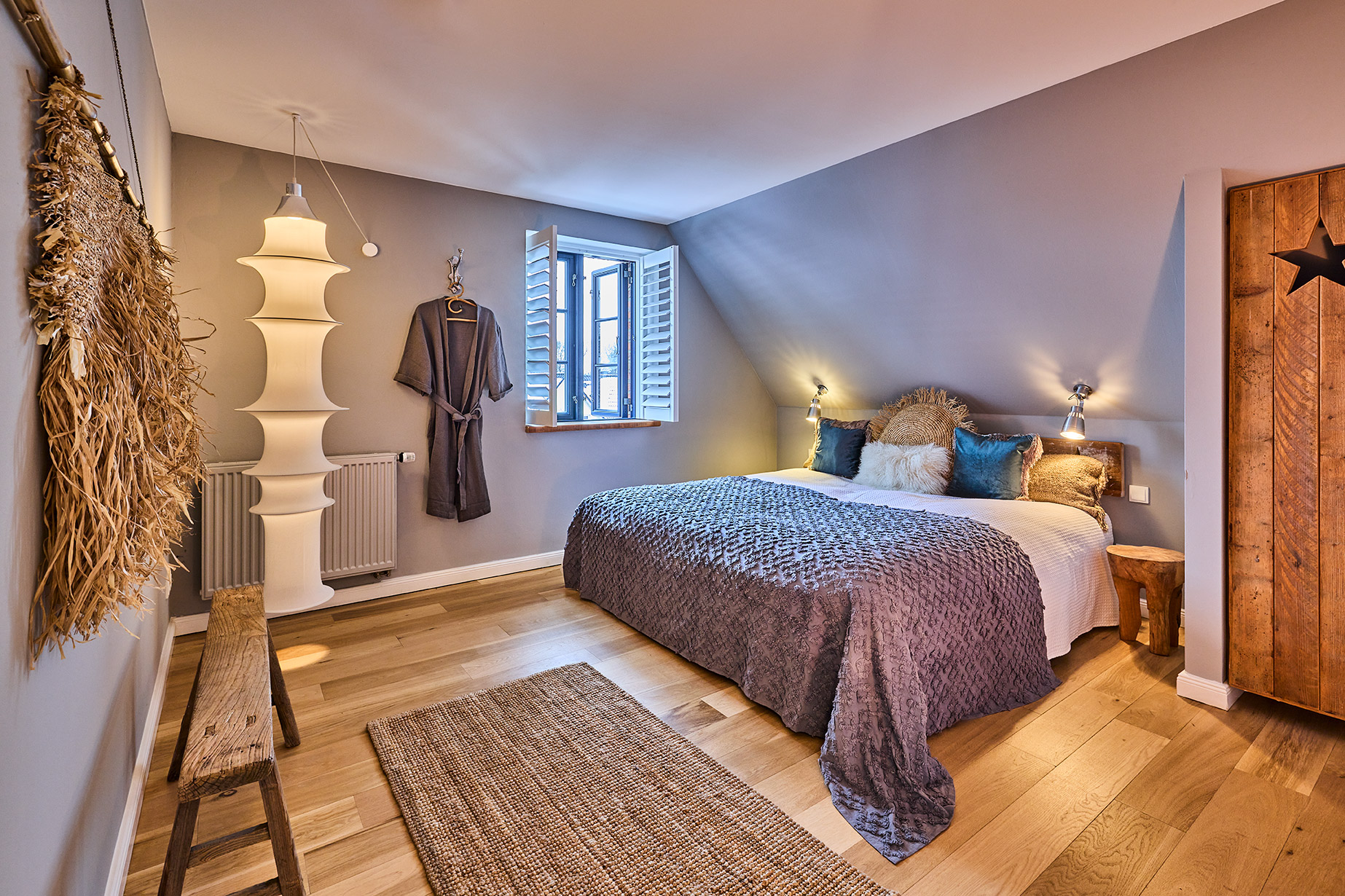 Gemütliches Schlafzimmer mit Doppelbett, Holzboden, Teppich und offenem Fenster.