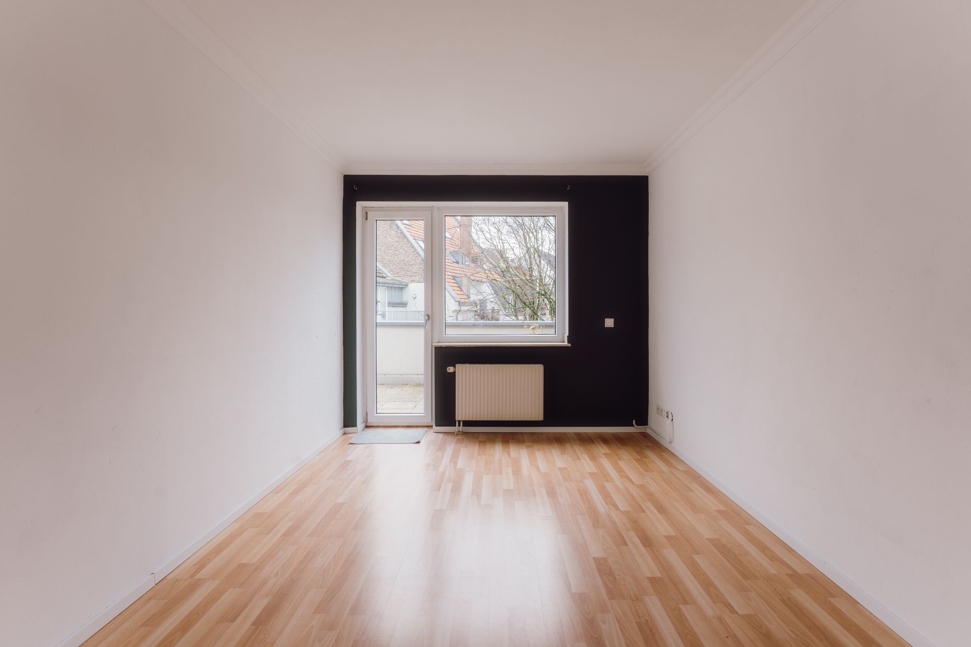 Leerer Raum mit Holzfußboden, weißem Wänden, Fenster und Tür zu einem Balkon.