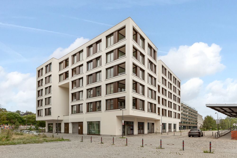 Modernes, mehrstöckiges Wohngebäude mit großen Fenstern auf einem gepflasterten Platz.