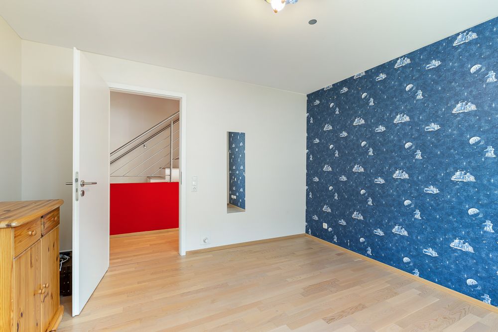 Zimmer mit Holzfußboden, blauer Tapete mit Muster und offen stehender Tür.