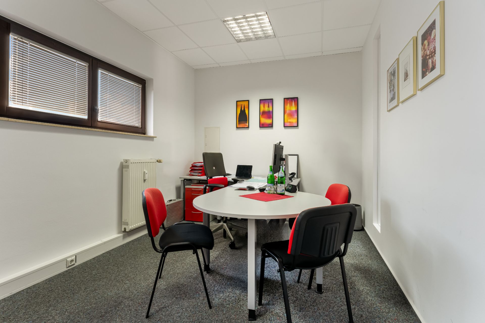 Helles Arbeitszimmer mit rundem Tisch, vier Stühlen und Computer auf dem Schreibtisch.