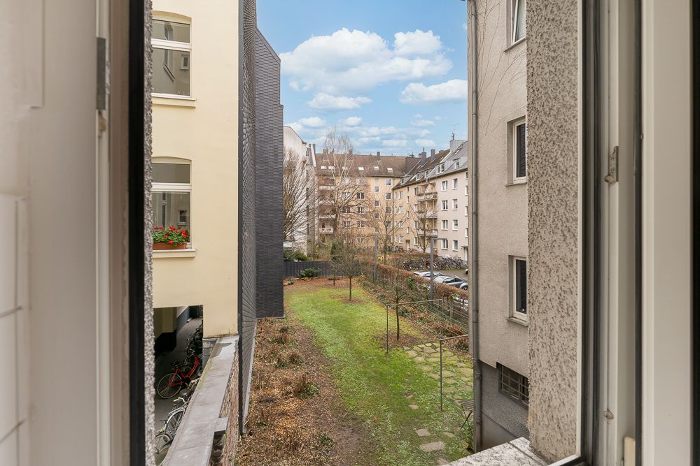 Blick aus dem Fenster auf einen grünen Innenhof mit Wäscheleinen und Wohngebäuden.
