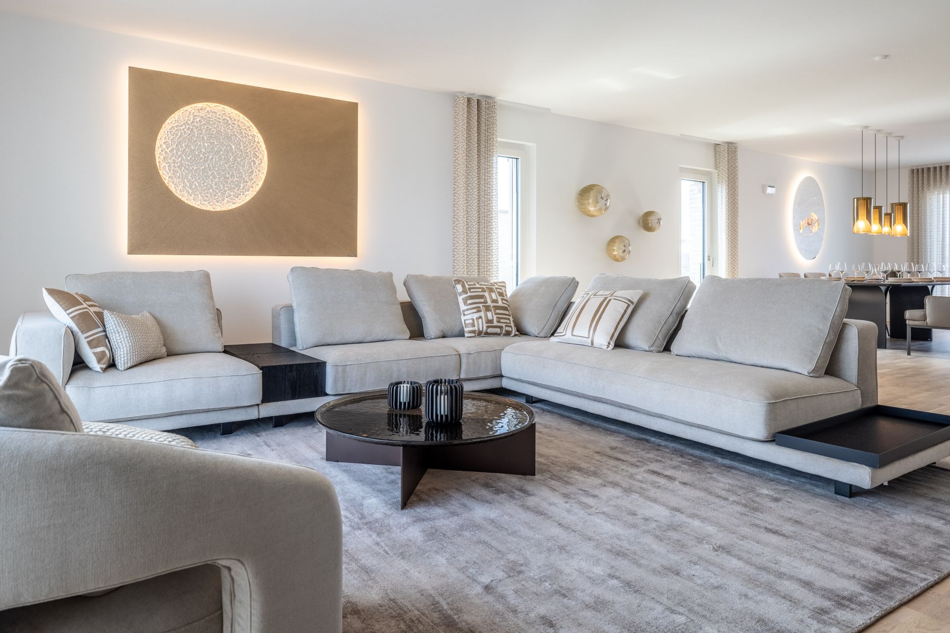 Modernes Wohnzimmer mit hellen Sofas, rundem Couchtisch und Wanddekoration, angrenzender Essbereich sichtbar.