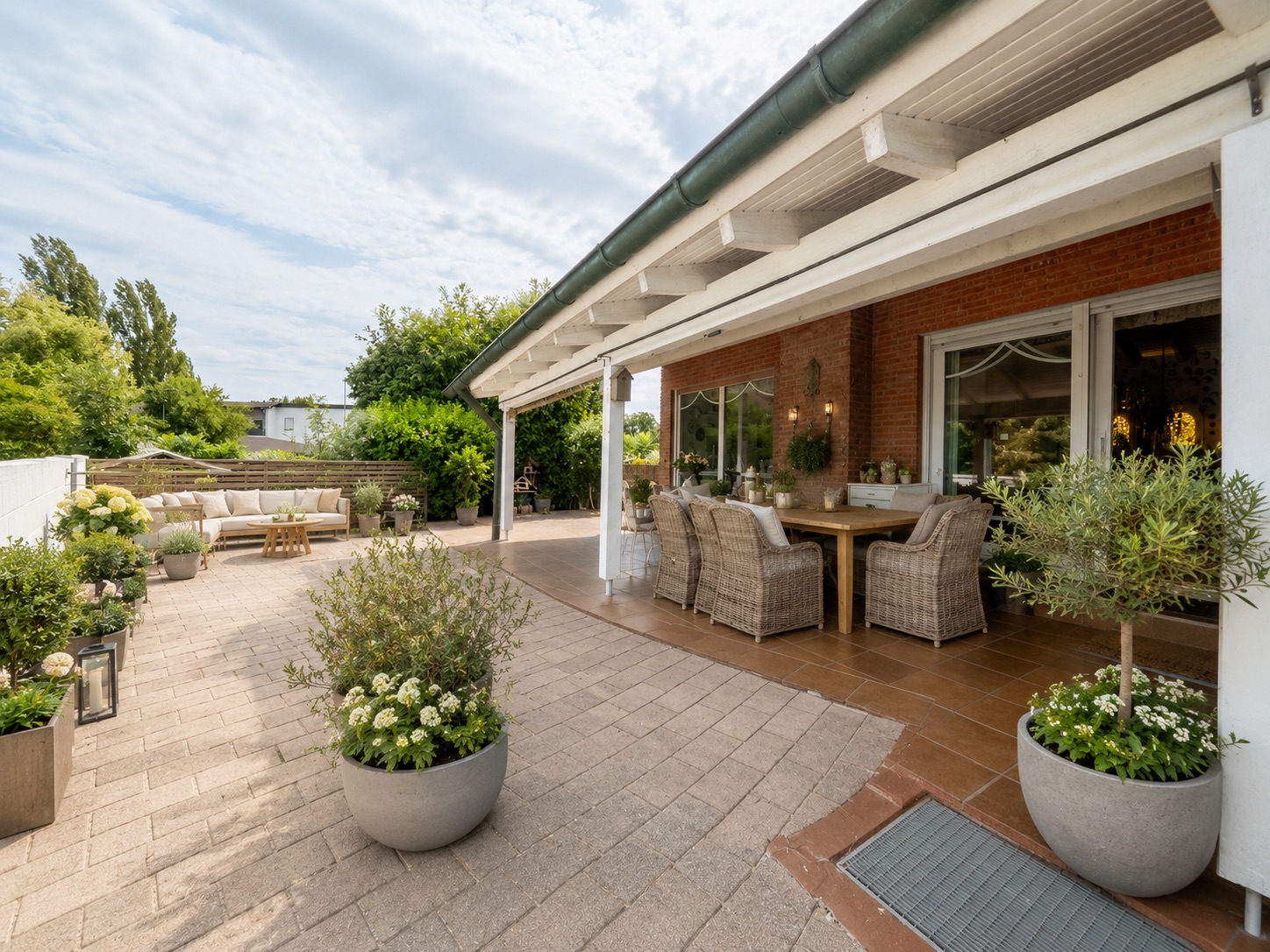 Große Terrasse mit Sitzmöbeln, Esstisch und vielen Pflanzen in Töpfen neben einem Haus.