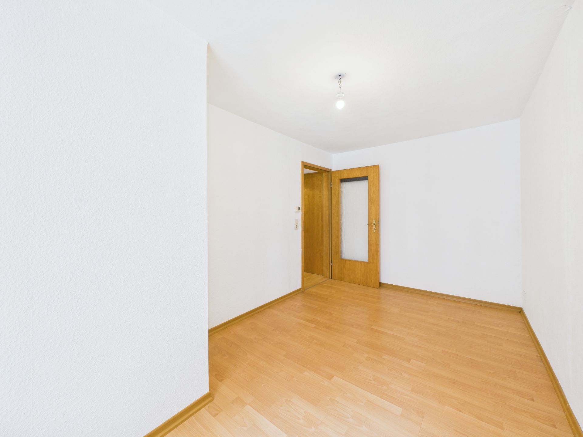 Leerer Raum mit hellem Holzfußboden, weißen Wänden und Holztür.