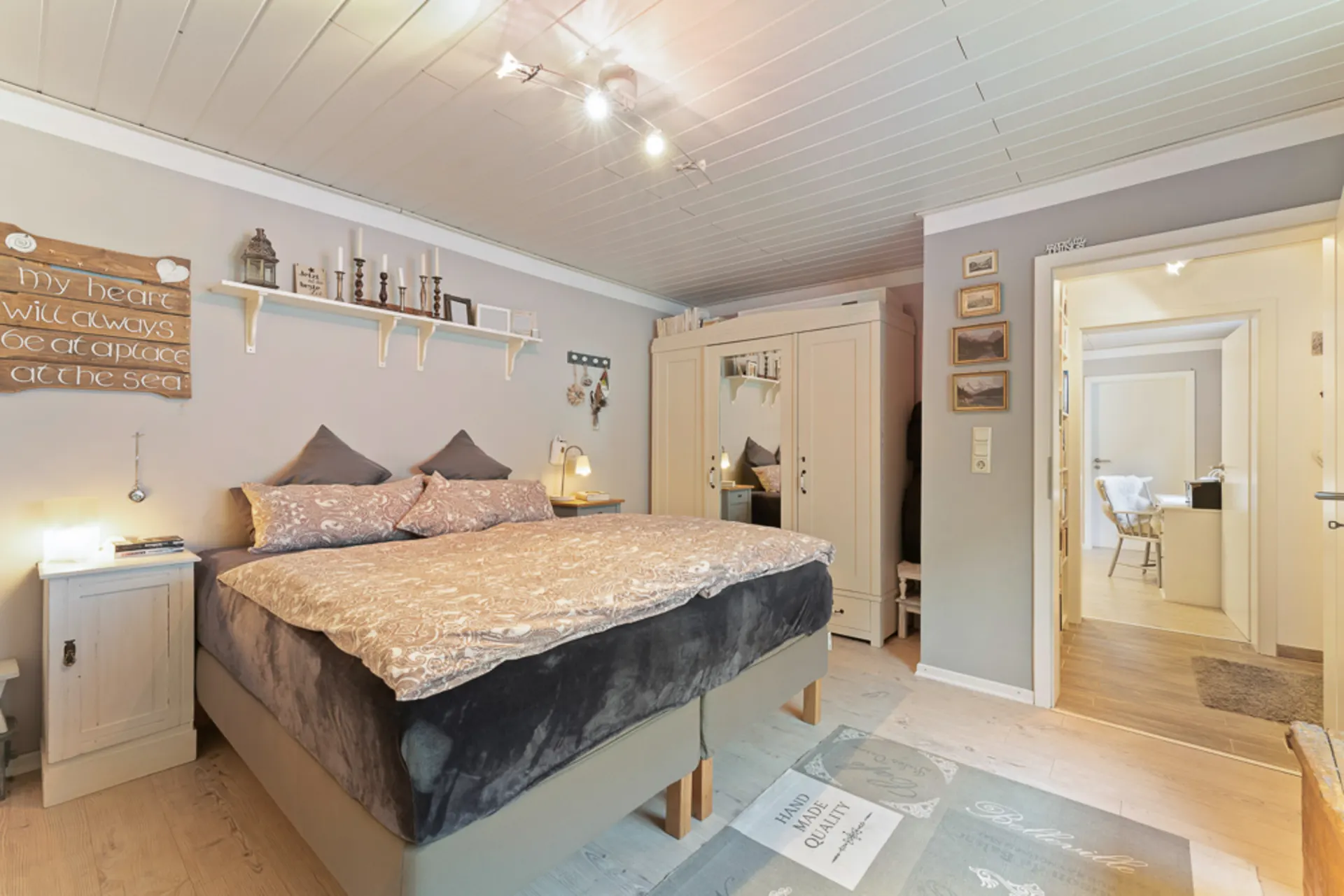 Helles Schlafzimmer mit Doppelbett, Nachttischen, Schrank und Wanddekoration.