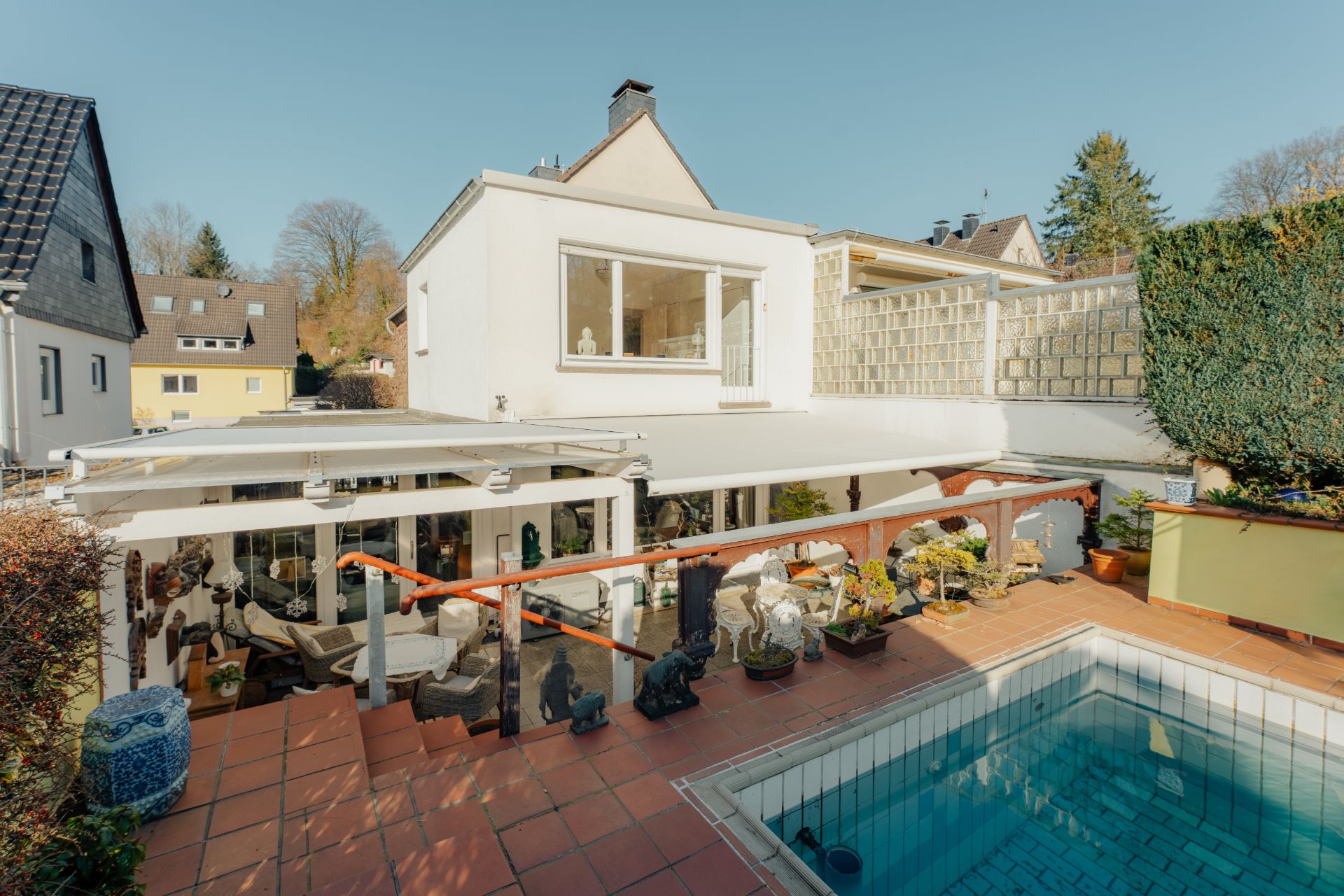 Weißes Wohnhaus mit Terrasse und kleinem Swimmingpool im Garten, umgeben von Pflanzen.
