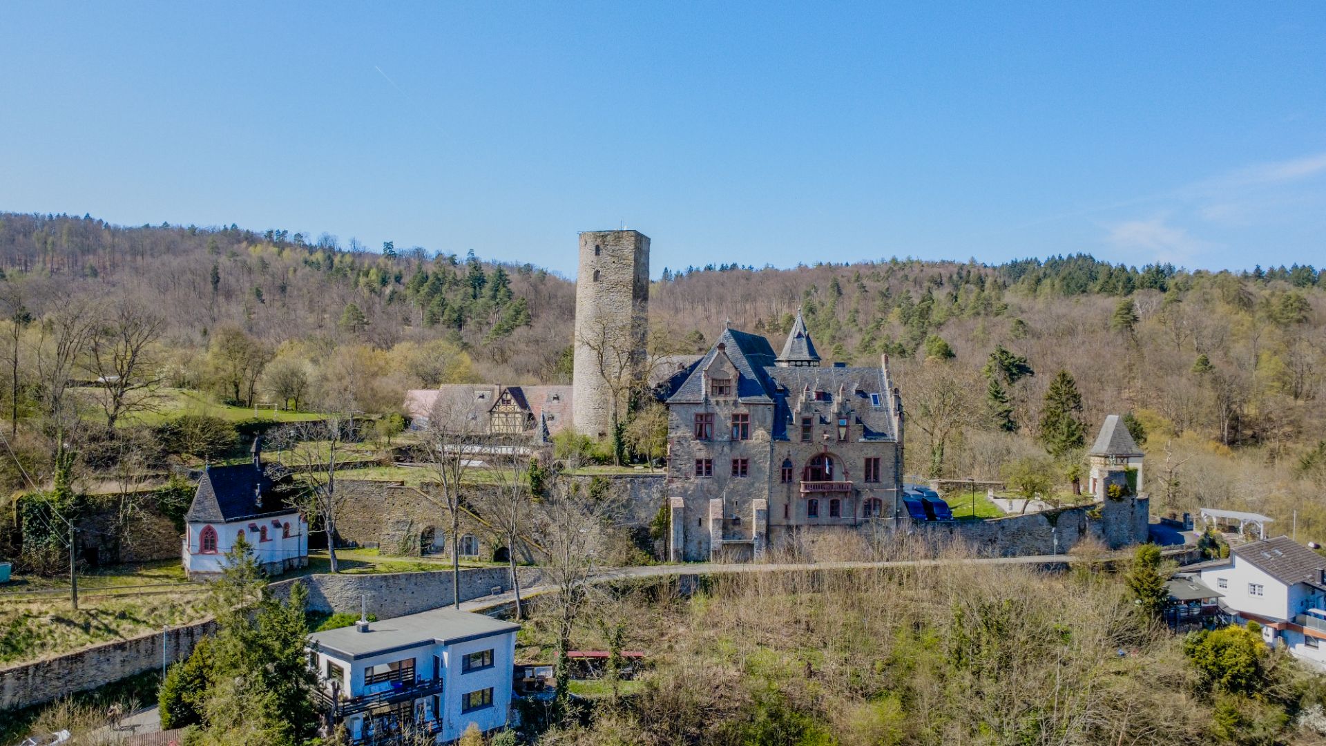 Großes Steingebäude mit Turm, umgeben von Bäumen und weiteren Häusern im Hintergrund.