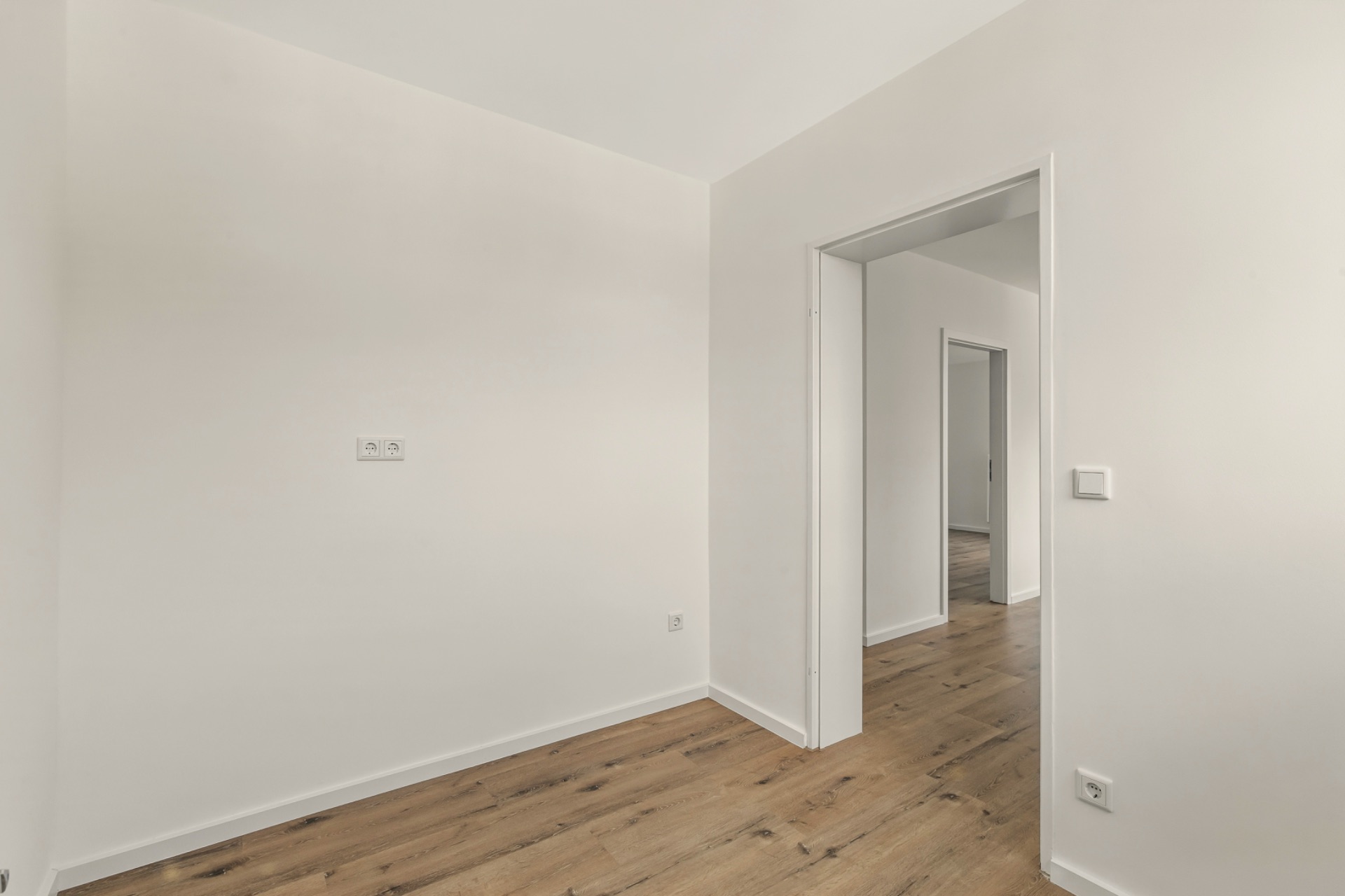 Heller Raum mit Holzboden und Durchgang zu weiteren Zimmern in einer Wohnung.