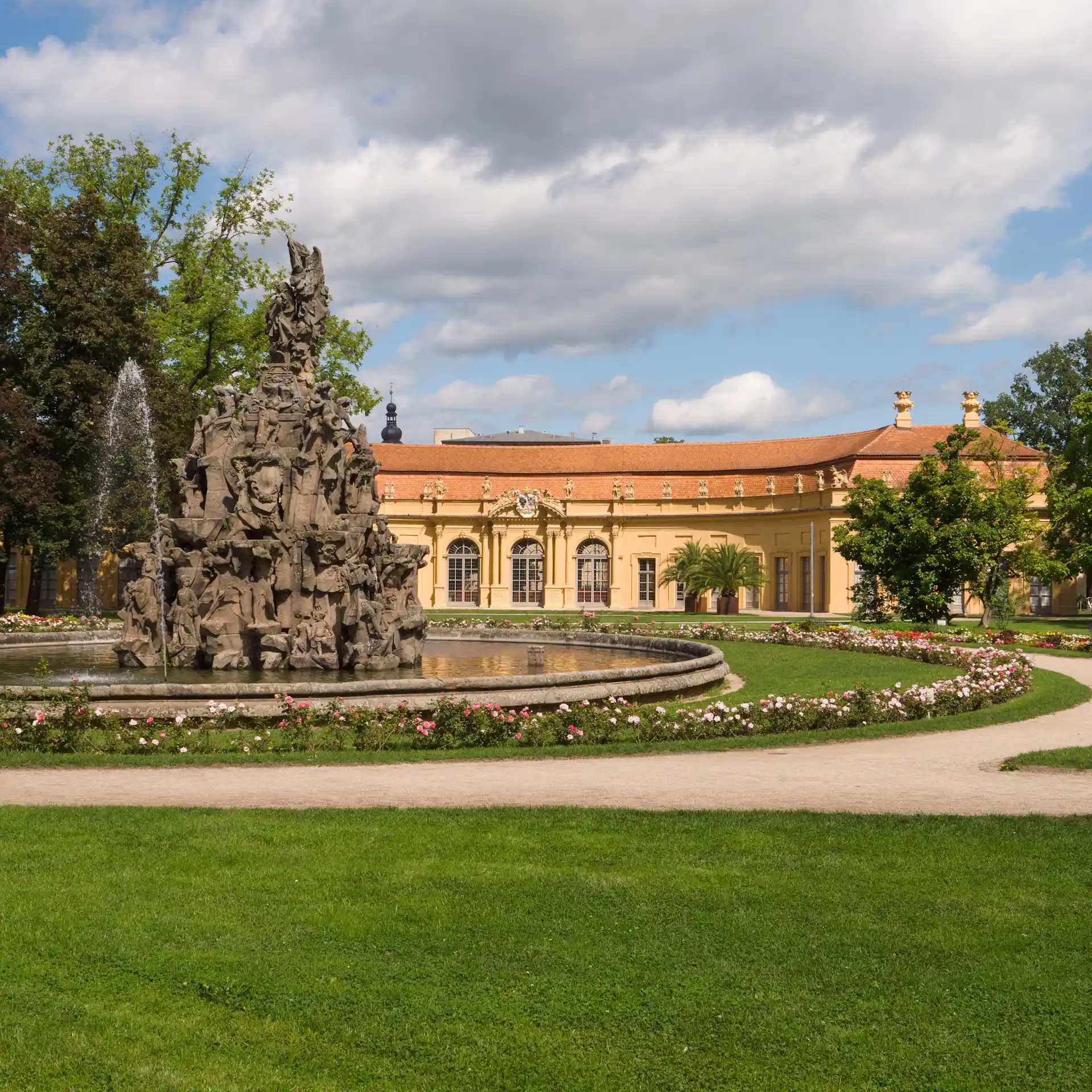 Großes, historisches Gebäude mit Turm und Uhr, davor Bäume und Straßenschilder.