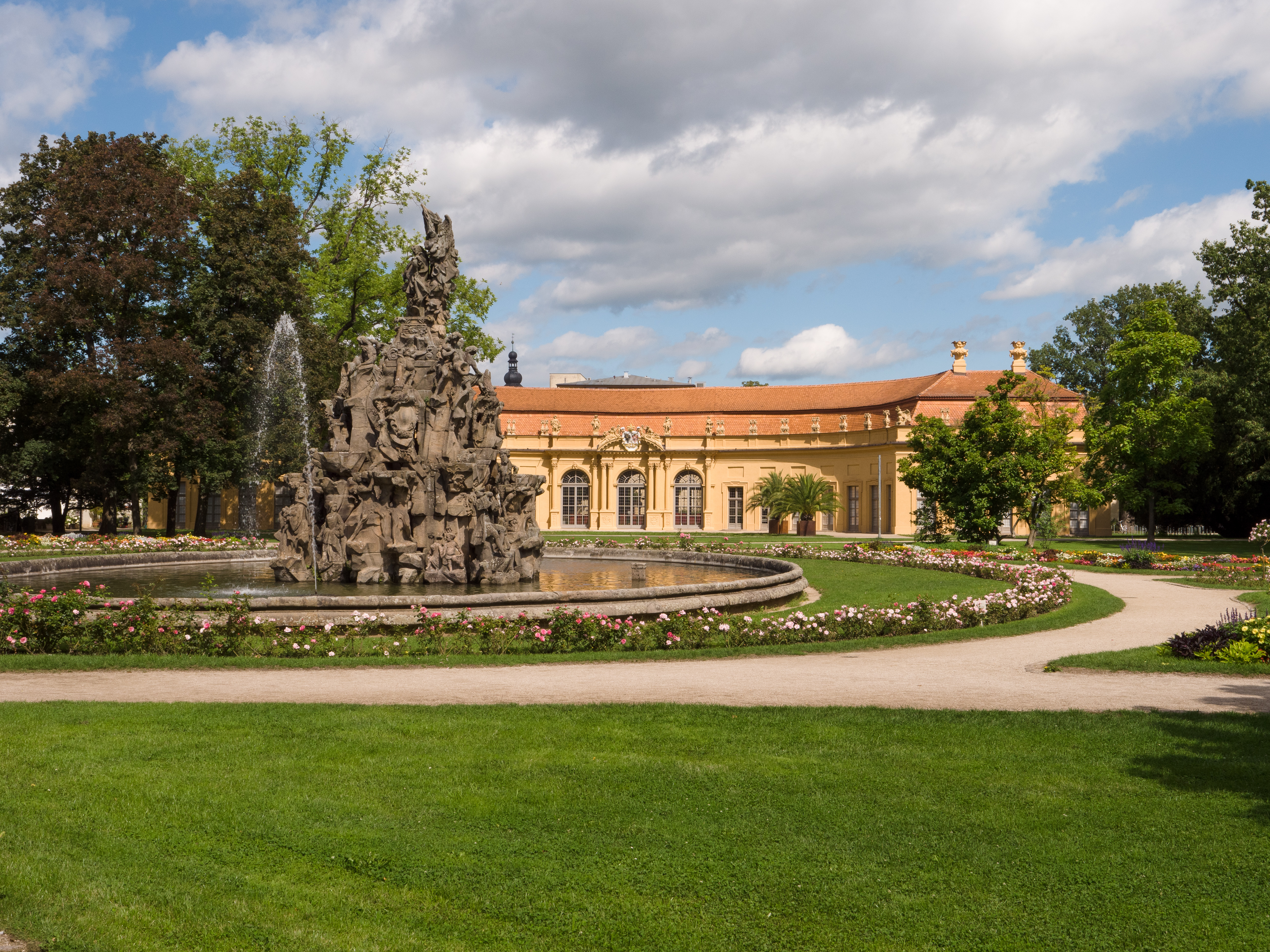 Großes, historisches Gebäude mit Turm und Uhr, davor Bäume und Straßenschilder.
