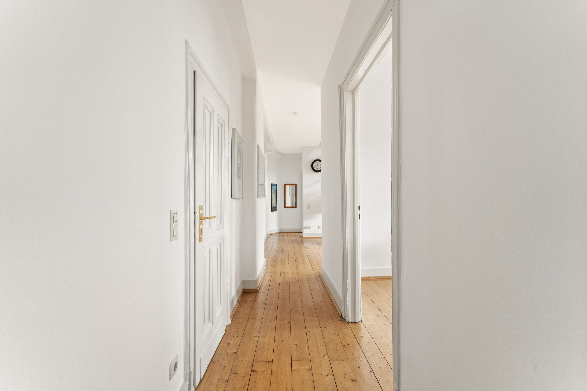 Heller Flur mit Holzboden, weißen Wänden und mehreren Türen in einer Wohnimmobilie.