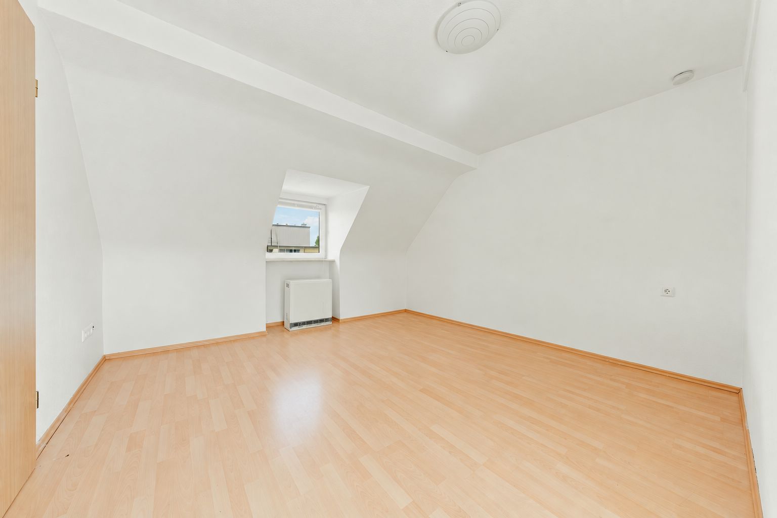 Heller leerer Raum mit Laminatboden, weißem Wänden und einem Dachfenster.
