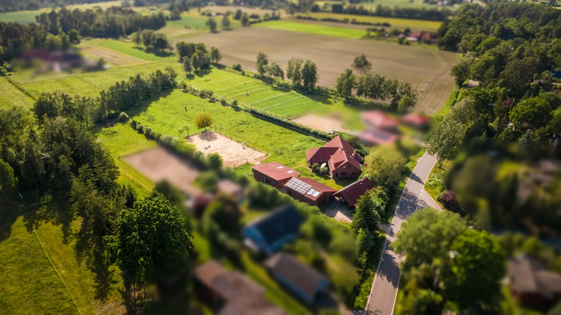 Luftaufnahme eines Wohnhauses mit Nebengebäuden und viel Grünfläche am Rand eines Dorfes.